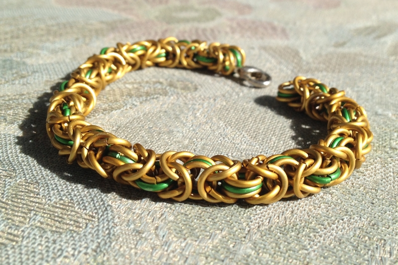A chainmail bracelet I made from gold and green galvanized aluminium rings in byzantine weave.